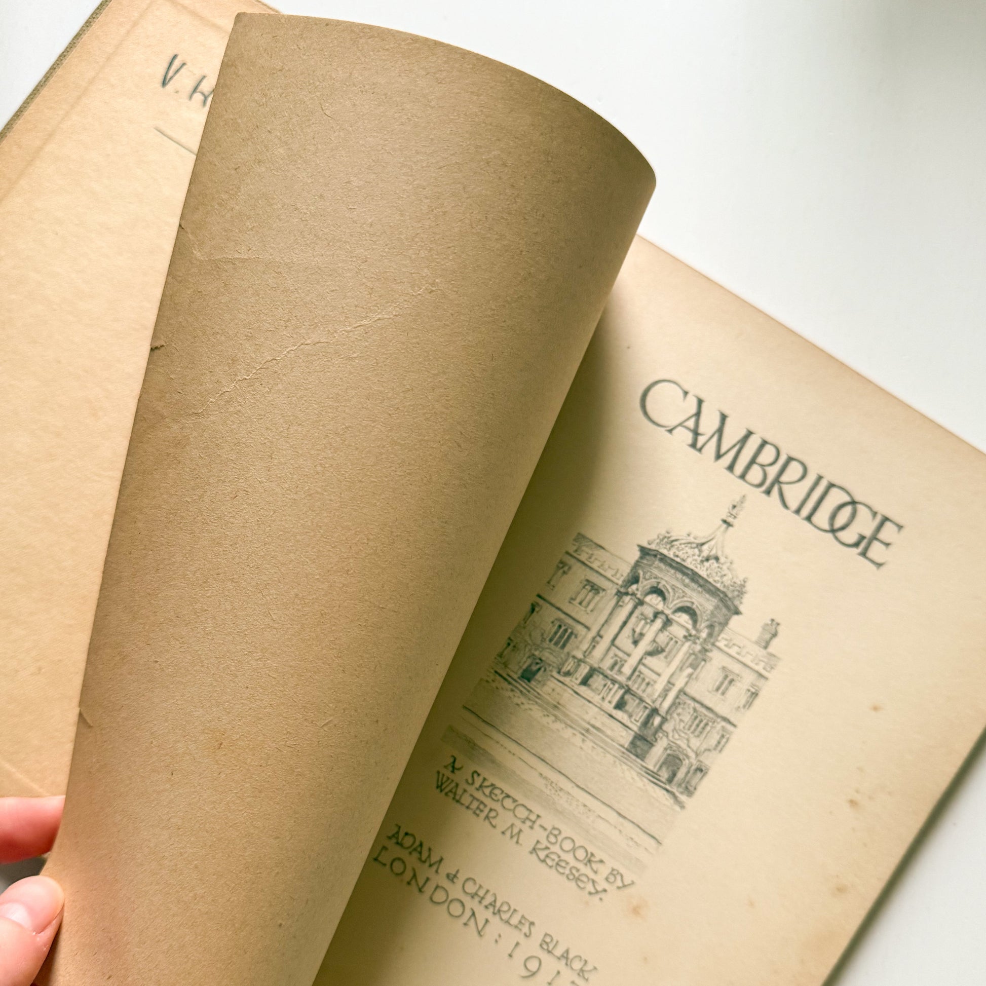 Close-up of an open book with 'Cambridge' printed on it, held by a hand.