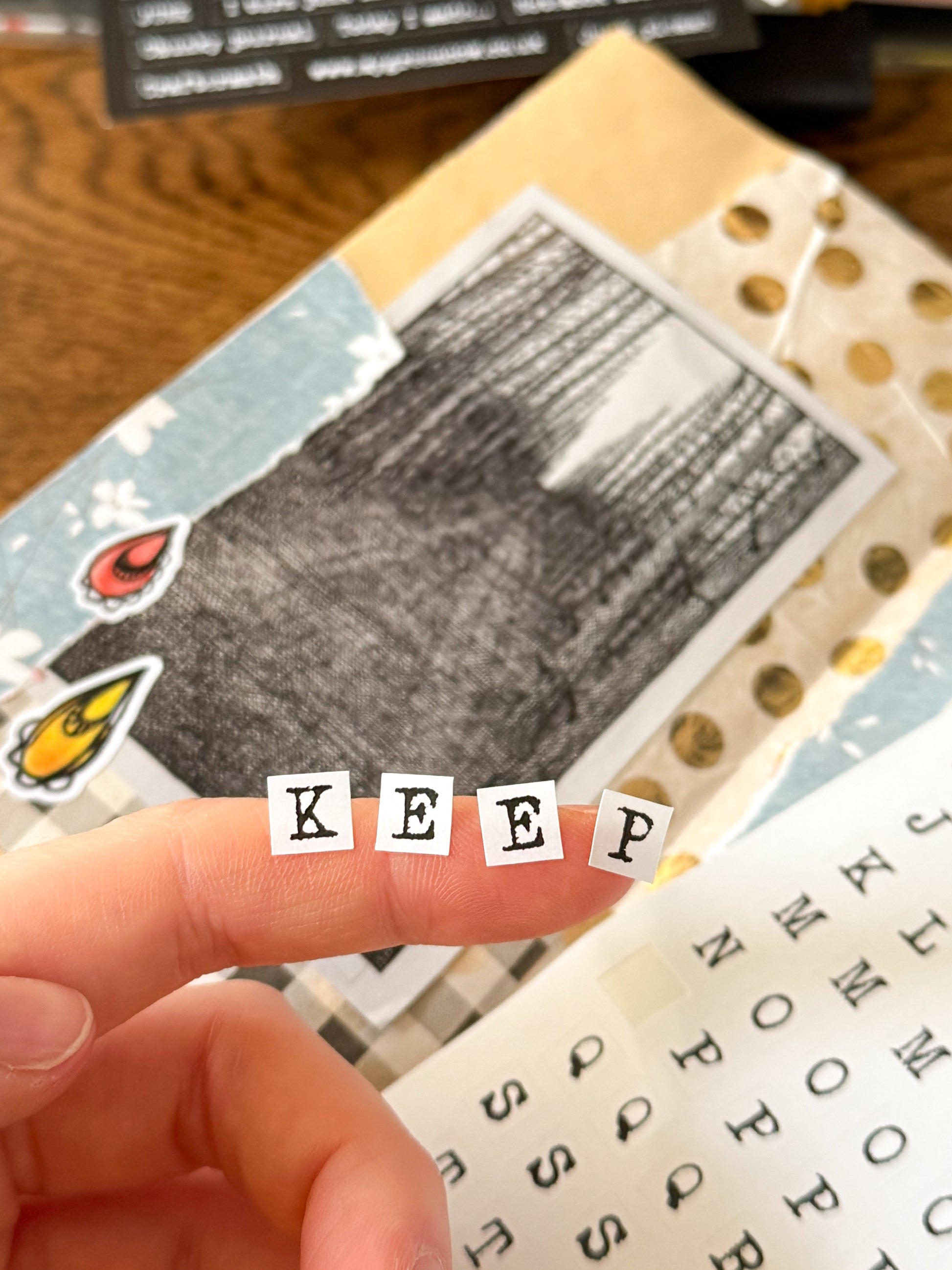Hand holding small typewriter alphabet stickers spelling 'KEEP' over a collage of images and text in a junk journal.